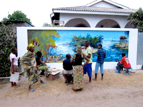 La famille et les voisins assistent à la création de la fresque murale «Le village de pêcheurs» réalisée par Rhode Makoumbou