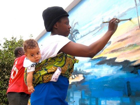 Sous les encouragements de son fils Quentin, Rhode Makoumbou réalise la fresque «Le village de pêcheurs»